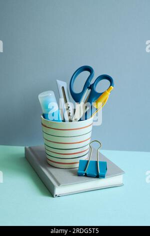 Writing supplies in pen holder and notebook on blue desk. blue wall background. workspace Stock Photo