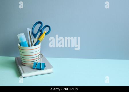 Writing supplies in pen holder and notebook on blue desk. blue wall background. workspace Stock Photo