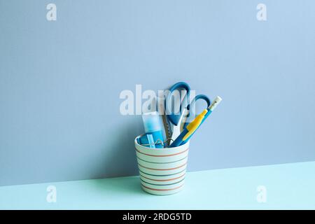 Writing supplies in pen holder on blue desk. blue wall background. stationery, office supply, workspace Stock Photo