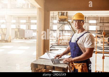 Cheerful male builder using laptop at construction site Stock Photo