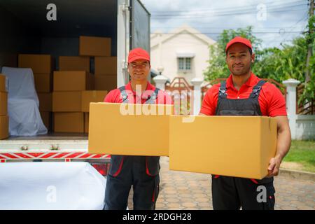 The House Removals company employees stand proudly behind the truck, boxes in hand, wearing smiles that reflect their commitment to a successful move. Stock Photo