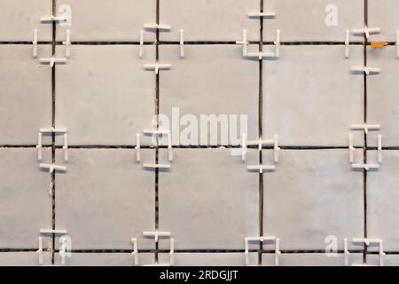 A front portrait of a tile wall under construction. The wall is being tiled with small rectangular tiles. There are still plastic white joint spacers Stock Photo