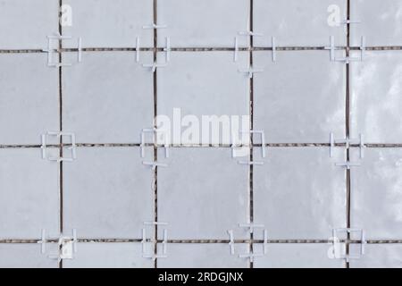 A front portrait of a tile wall under construction. The wall is being tiled with small rectangular ceramic tiles. There are still white plastic joint Stock Photo