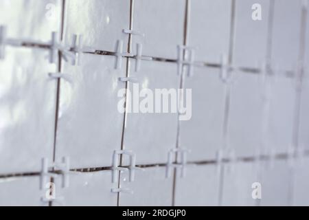 A tile wall under construction. The wall is being tiled with small bumpy rectangular ceramic tiles. There are still plastic white joint spacers in bet Stock Photo