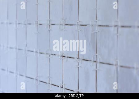 A portrait of a ceramic tile wall under construction. The wall is being tiled with small rectangular tiles. There are still white plastic joint spacer Stock Photo