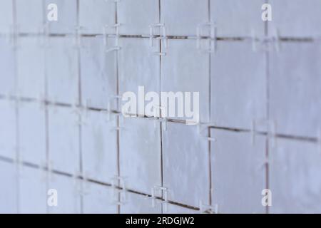 A portrait of a tile wall under construction. The wall is being tiled with small ceramic rectangular tiles. There are still plastic white joint spacer Stock Photo