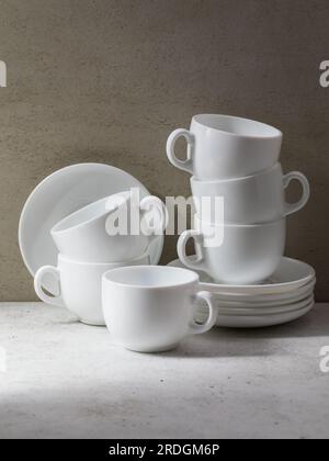 A set of 6 pairs of white ceramic dishes, cups and saucers for tea or coffee on the table Stock Photo