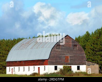 Rustic barn with weathered red wood has tin roof and block base.  Barn is located in Upper Peninsula, Michigan on the Keweenaw Peninsula. Stock Photo