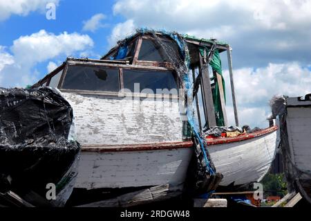 Ruins of old fishing boat sits near Lake Superior in Ripley, Upper Peninsula, Michigan.  Wooden boat has cracked and peeling paint, broken window and Stock Photo