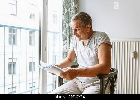 man sitting at window reading folder with documents Stock Photo