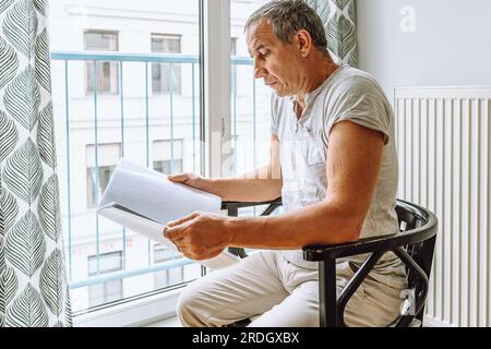 man sitting at window reading folder with documents Stock Photo