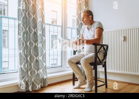 man sitting at window reading folder with documents Stock Photo