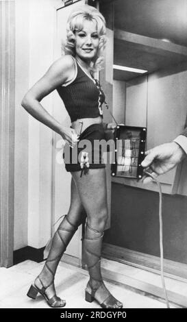 Miami, Florida:  September, 1971 An airline stewardess instructor demonstrates how the new Friskem device being installed at Eastern Airline passenger gates can detect weapons. The glowing black box at right shows she has a metal knife stuck in her hot pants. Stock Photo