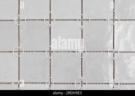 A front portrait of a tile wall under construction. The wall is being tiled with small rectangular tiles. There are still white plastic joint spacers Stock Photo