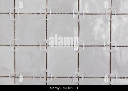 A front portrait of a tile wall under construction. The wall is being tiled with small rectangular ceramic tiles. There are still plastic white joint Stock Photo