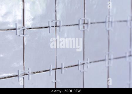 A close up of a tile wall under construction. The wall is being tiled with small bumpy rectangular ceramic tiles. There are still plastic white joint Stock Photo