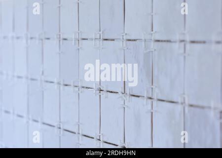 A portrait of a ceramic tile wall under construction. The wall is being tiled with small bumpy rectangular tiles. There are still plastic white joint Stock Photo