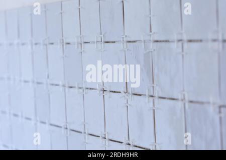 A portrait of a ceramic tile wall under construction. The wall is being tiled with small rectangular tiles. There are still plastic white joint spacer Stock Photo