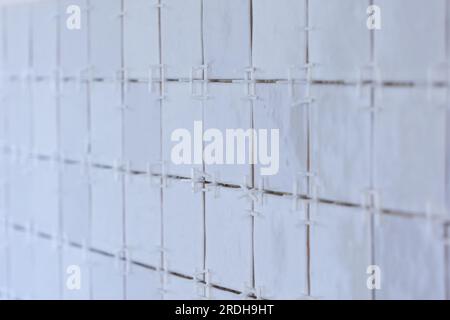 A portrait of a tile wall under construction. The wall is being tiled with small bumpy rectangular ceramic tiles. There are still plastic white joint Stock Photo