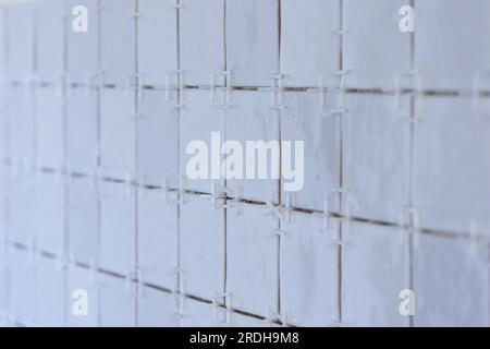 A portrait of a tile wall under construction. The wall is being tiled with small ceramic rectangular tiles. There are still white plastic joint spacer Stock Photo
