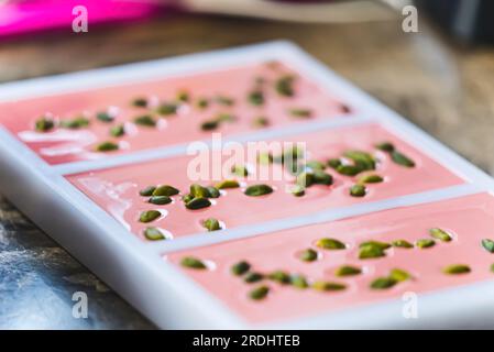 Pink chocolate bars in moulds. Ruby chocolate production process. Modern chocoat with pistachios. Chocolate moulds isolated on brown kitchen counter. High quality photo Stock Photo