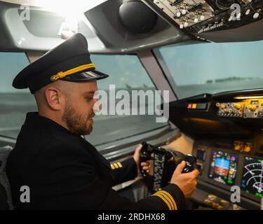 Caucasian bearded man smiling while sitting in a flight simulator. Pilot in the cockpit. Stock Photo
