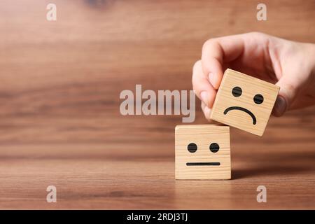 Complaint. Woman choosing cube with drawn sad face instead of another one with happy on wooden table, closeup. Space for text Stock Photo