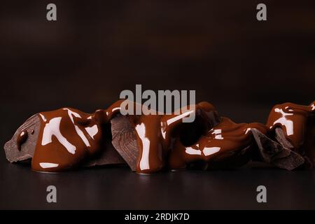 pieces of dark chocolate covered with melted cocoa on black table. sweet dessert Stock Photo