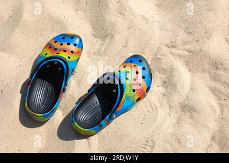 Ukraine, Kyiv - July 04. 2022: Сolorful crocs footwear on the beach, vacation background. Сolorful trendy croc beach shoes. Vacation concept. Travel v Stock Photo