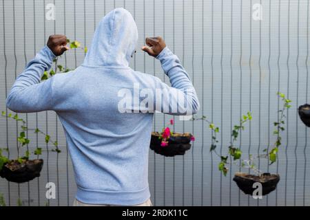 Rear view of african american man wearing grey hooded sweatshirt against white fence, copy space Stock Photo