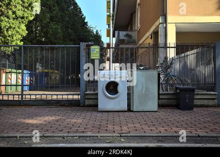 Broken  washing machine and refrigerator on the pavement of a street in a residential area at sunset Stock Photo