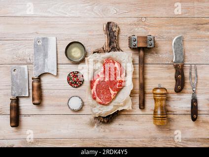 Raw beef rib eye with meat utensils set on wooden background. Fork,knife,meat cleavers with tenderizer and salt,pepper,chopping board and pepper mill. Stock Photo