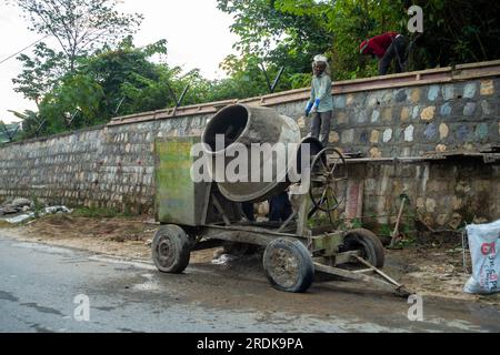 June 28th 2023, Uttarakhand, India. Construction of stone retaining wall along side road with mixture machine and workers on site. Stock Photo