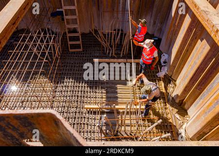 Shot above on workers surrounded by metal piles, who are installing basic profile made of bended rusty reinforcing rods in square shape for bridge fou Stock Photo