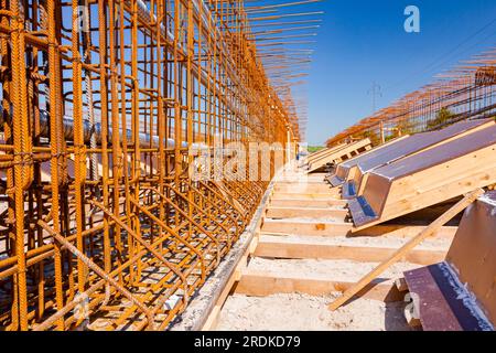 Girder, bridge skeleton, reinforcement, installed vertical crossed rusty armature rods and pile of painted wooden molds on the building site. Stock Photo