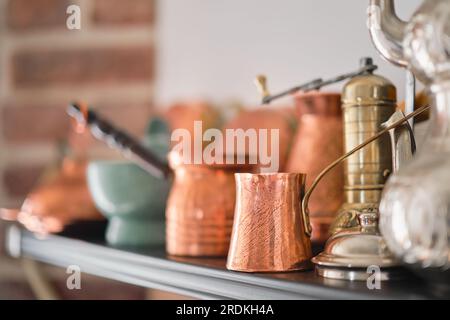 Handmade copper cezve, Turkish traditional tableware on a shelf in the kitchen at home or in a restaurant, selective focus Stock Photo
