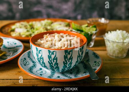 Pozole served in a deep dish, with salsa and vegetables on a wooden table. Typical Mexican food. Stock Photo