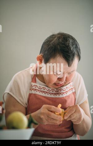 Elderly woman with Down syndrome finds joy and independence in peeling mandarin Stock Photo