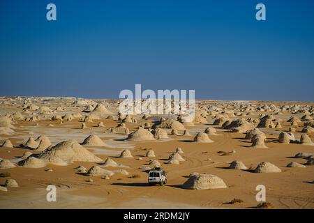 A jeep seen driving through various calcified limestone rocks in the White Desert, Egypt. From erosion of volcanos and a quartz mountain, to weathering rocks and white chalk rock formations, Black and White Desert is part of the Frarafra depression in the Sahara Desert and locates at the Western part of Egypt. The vast desert links to main roads that are close to the Libyan-Egyptian border where it is now heavily armed with military presence. The bizarre natural landscape rising from an ocean floor million years ago is now left with karst limestone formations that resembles to the surface of o Stock Photo