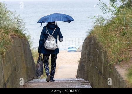 Zinnowitz, Germany. 22nd July, 2023. Tourists walk in the rain on the beach promenade of the seaside resort of Zinnowitz on the island of Usedom. Meteorologists are expecting changeable weather on the Baltic Sea in the coming days as well. The weather does not mean it at present well with the vacation country Mecklenburg-Western Pomerania. Since the trend is to book at short notice, the weather has an influence on the decision where to go on vacation, said the managing director of the state tourism association. Credit: Stefan Sauer/dpa/Alamy Live News Stock Photo