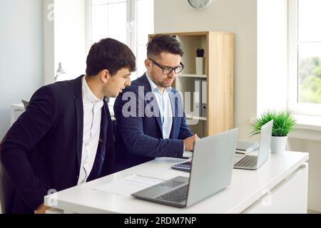 Two male colleagues working in pairs on laptops in office of financial business company. Stock Photo