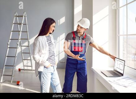 Architect or engineer shows blueprints on laptop and discusses house construction with customer Stock Photo