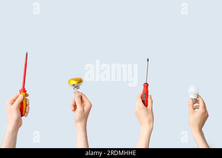 Electrician hands with light bulbs and tools on grey background Stock Photo