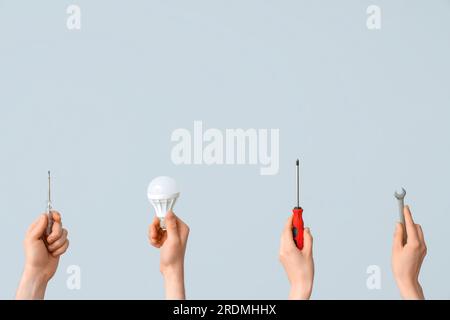Electrician hands with light bulbs and tools on grey background Stock Photo