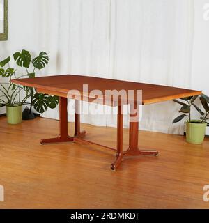 Beautiful late-century extended teak dining table. Vintage wooden furniture. Interior scene with luxurious white curtains and houseplants. Stock Photo