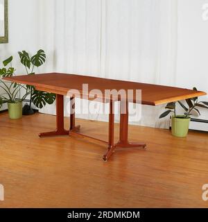 Beautiful late-century extended teak dining table. Vintage wooden furniture. Interior scene with luxurious white curtains and houseplants. Stock Photo