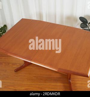 Beautiful late-century extended teak dining table. Vintage wooden furniture. Interior scene with luxurious white curtains and houseplants. Stock Photo