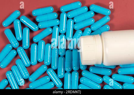 Blue antibiotic capsule pills texture with white bottle. Pharmaceutical production. Global health. Resistance to antibiotic drugs. Gelatin capsule pil Stock Photo