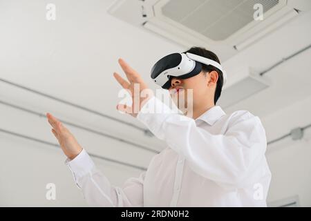 Businessman wearing virtual reality goggles headset and touching AI world, Happy man touching digital pixel screen in modern office, Futuristic Stock Photo