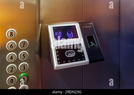 The fingerprint access control terminal with face recognition function installed in the elevator of the business center monitors attendance in real ti Stock Photo
